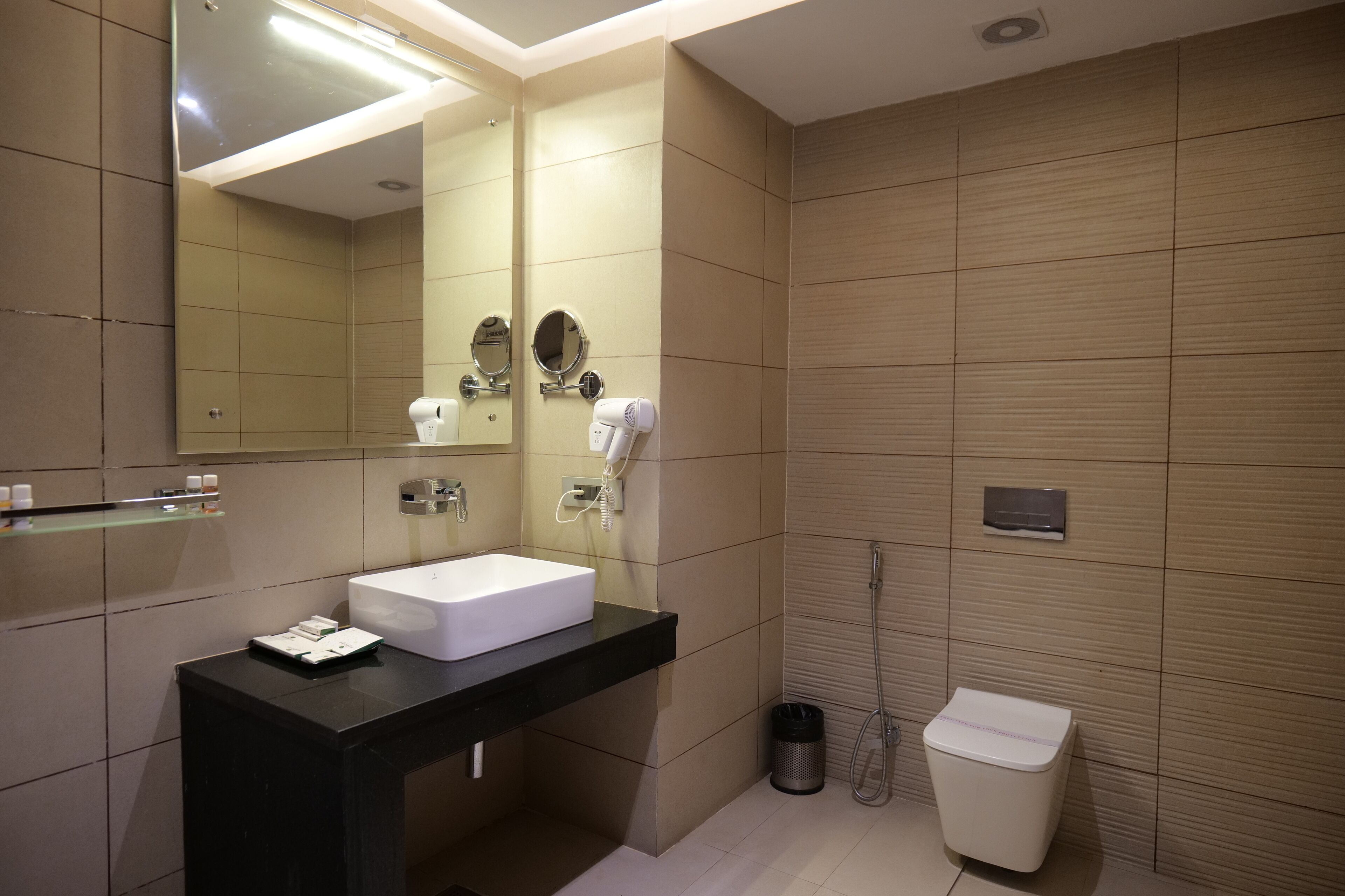 A modern bathroom with a large mirror, a white sink, a black countertop, a handheld showerhead, and a white toilet.