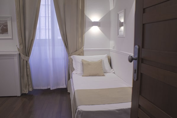 A hotel room with a bed, curtains, a wall-mounted light, and a door. - Palazzo Sant'Elena (Foggia)