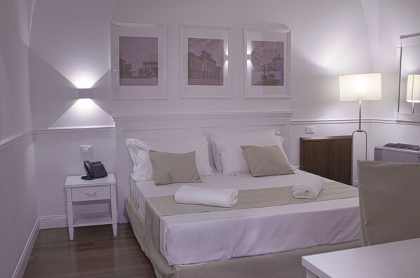 Una habitación de hotel con una cama bien hecha, una mesita de noche con teléfono, lámpara y cuadros en la pared.