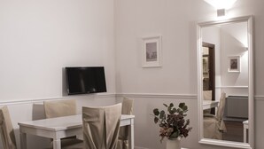 A dining area with a white table and chairs, a flat-screen TV mounted on the wall, a large mirror, and a vase with flowers. - Palazzo Sant'Elena (Foggia)