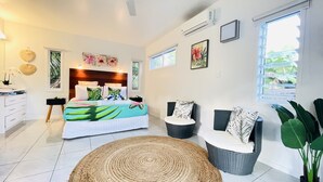 Un dormitorio moderno con una cama grande, una zona de estar con una silla y una mesita, y un ventanal con vistas a zonas verdes.