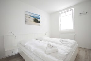 Un dormitorio con cama, mesita de noche, ventana y un cuadro colgado en la pared.