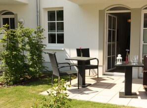 Un patio al aire libre con una mesa y sillas, un jardín pequeño y un edificio con ventanas grandes.