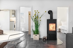 A modern living room with a round glass table, chairs, a potted plant, a black wood-burning stove, and a white sofa.