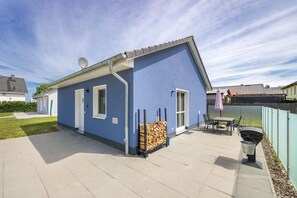 A blue house with a patio, a grill, and a stack of firewood.