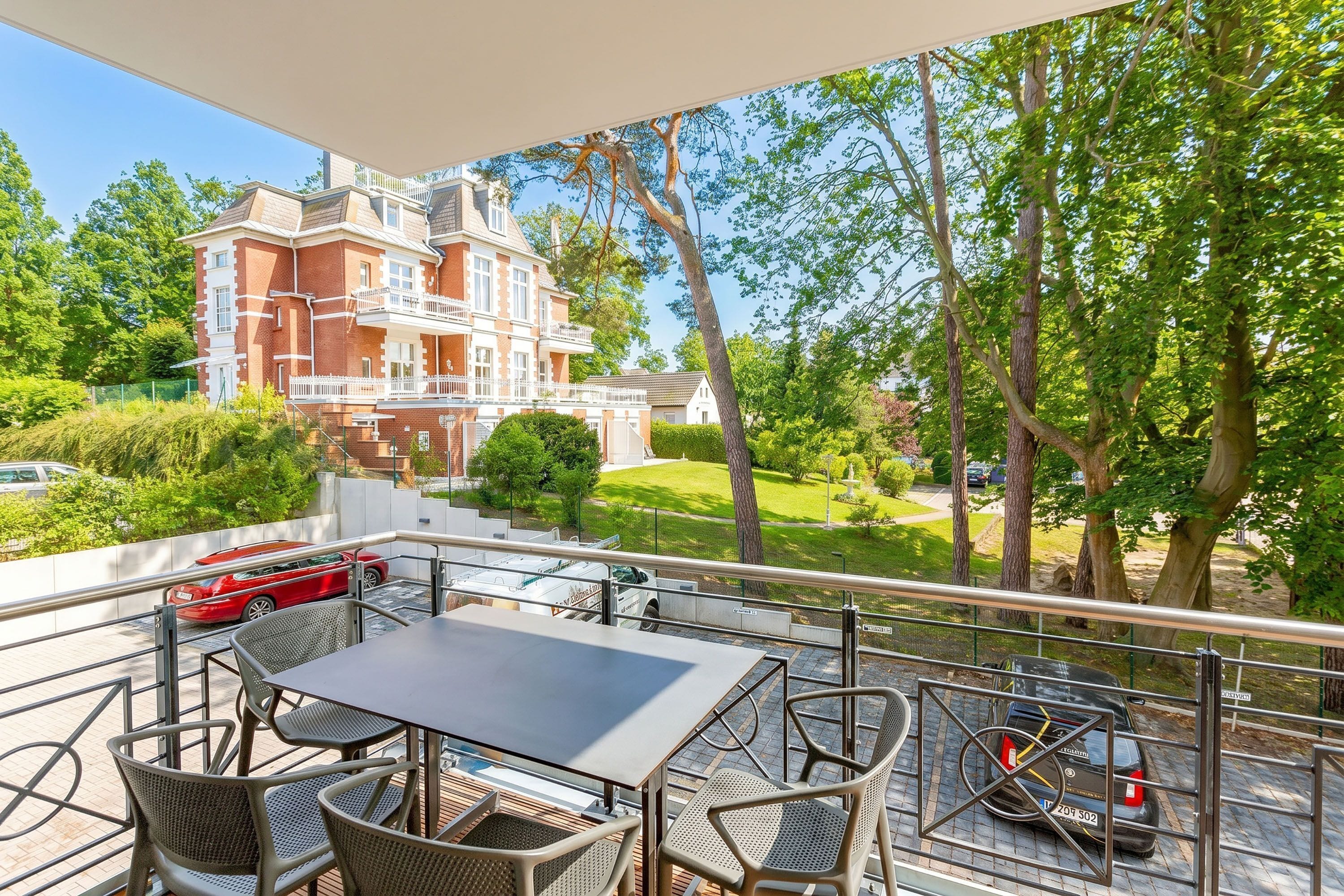 A balcony with outdoor furniture, a view of a large building, and parked cars.