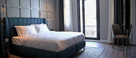A modern bedroom with a large bed, a chair, a window with a view, and a door.