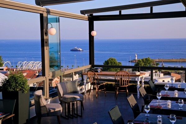 Una terraza con mesas y sillas con vista al mar, un barco en la distancia y un faro al fondo.