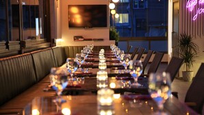 A restaurant with a long dining table set for a meal, a television mounted on the wall, and a neon sign on the wall. - Hotel Bronte (Istanbul)
