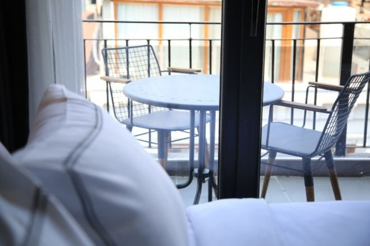 A balcony with a round table and metal chairs, overlooking a street.