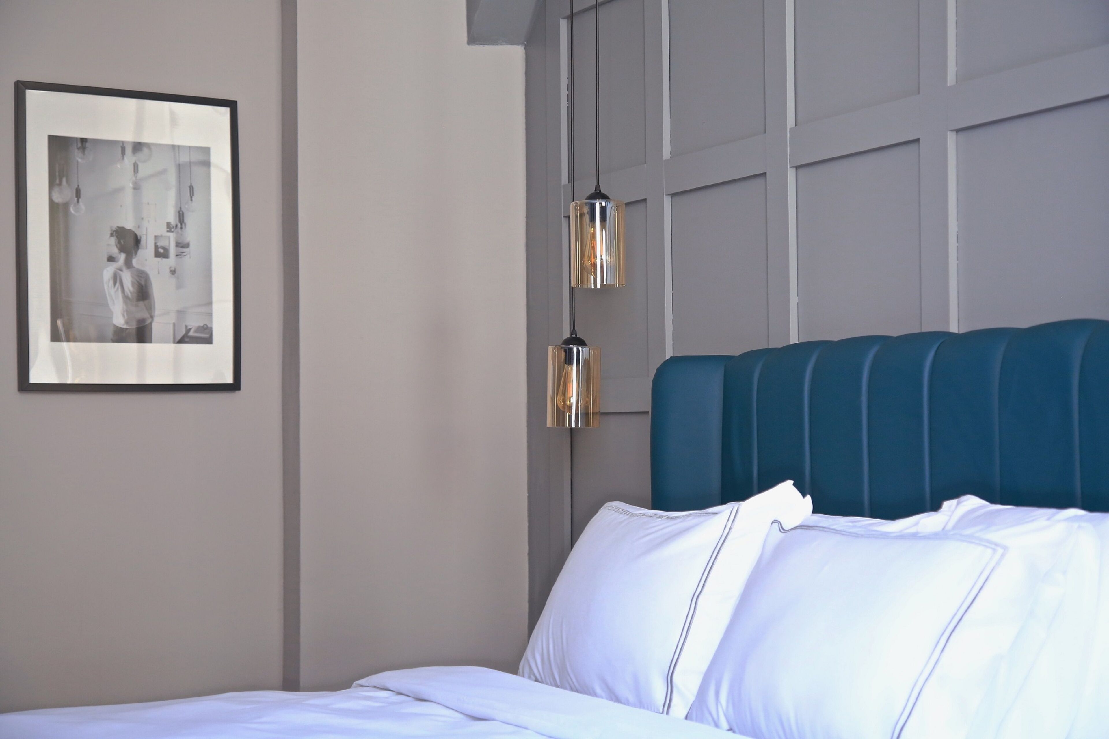 A hotel room with a bed, a framed photograph on the wall, and pendant lights.
