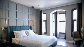 A modern bedroom with a large bed, a nightstand, a chair, and a view of the outside through a window. - Hotel Bronte (Istanbul)
