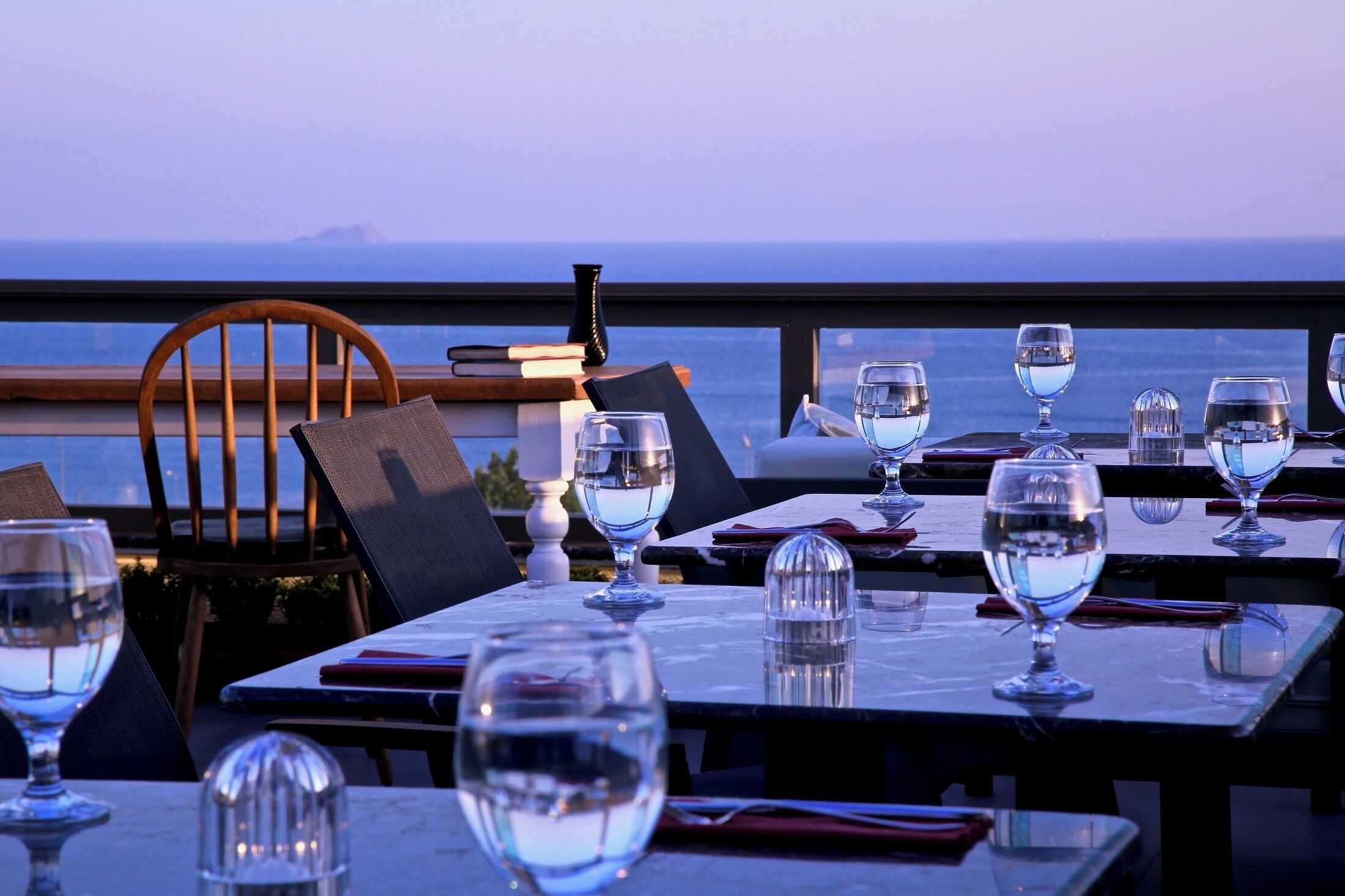 A dining area with tables set for two, overlooking the ocean.