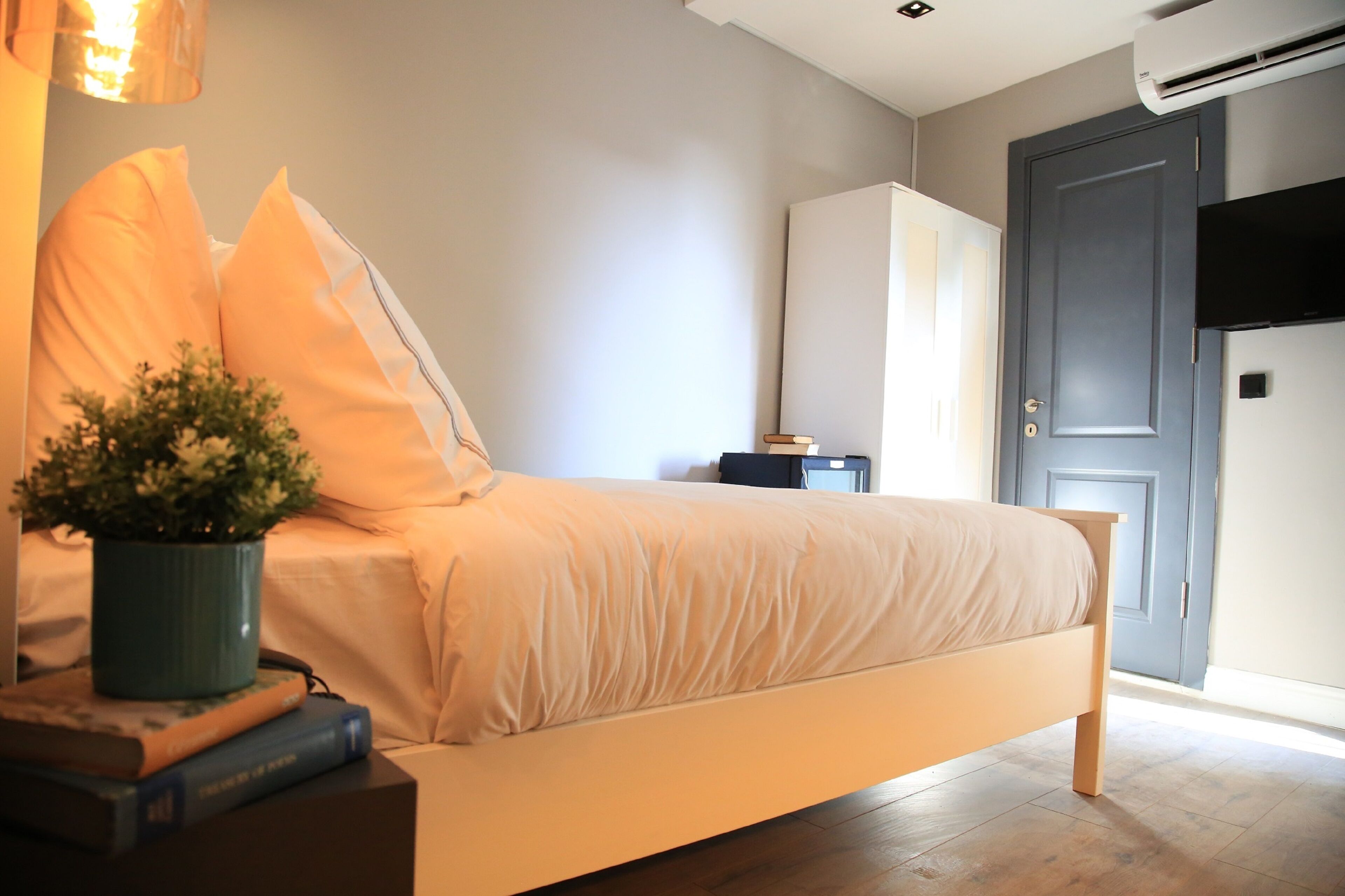 A bedroom with a bed, bedside table, lamp, and a potted plant.