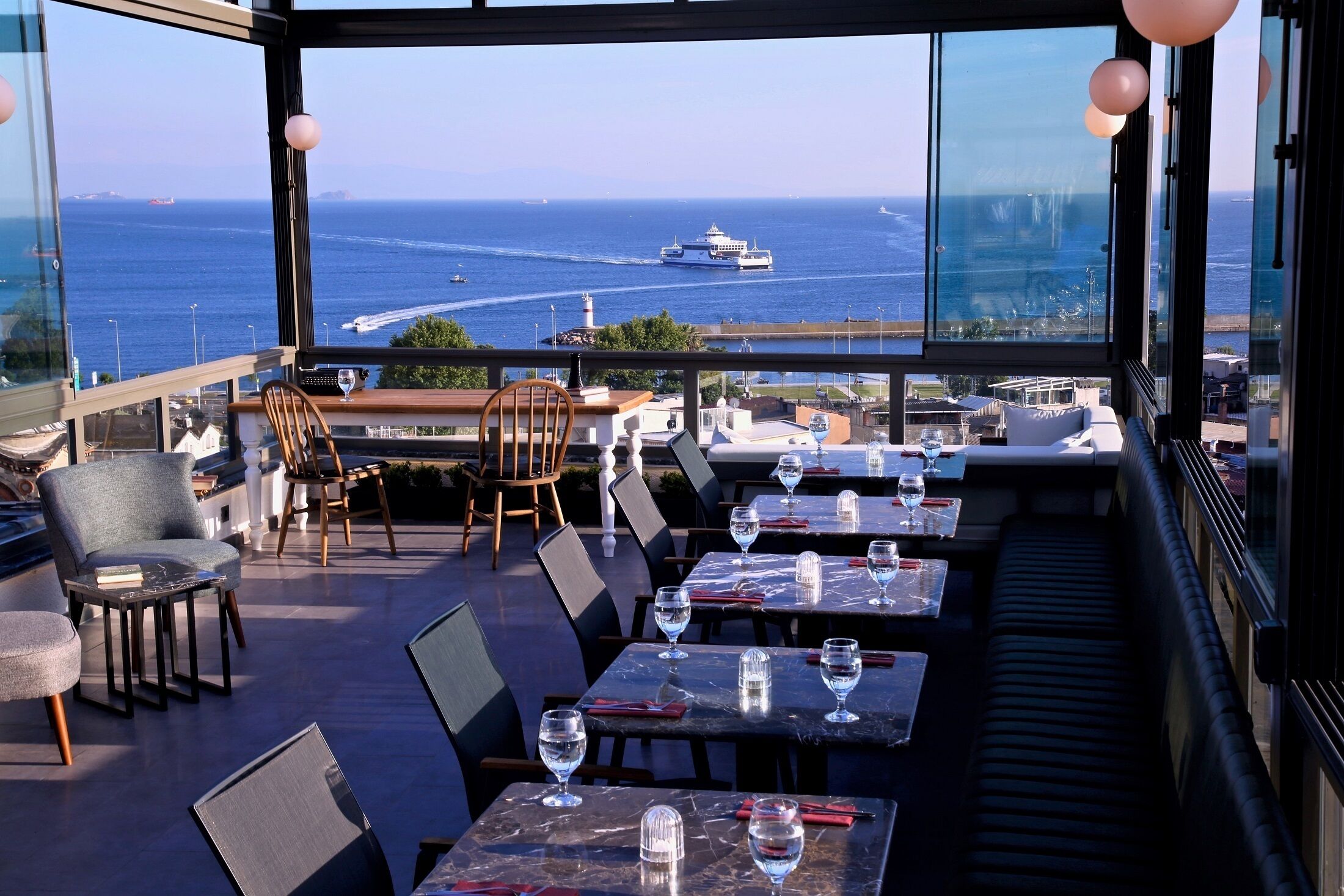 Terraza en la azotea con mesas y sillas, con vistas al mar y un crucero.