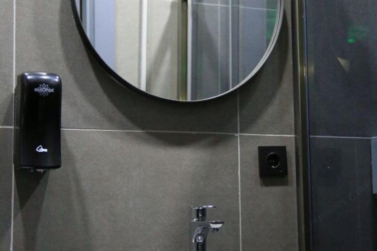 Een toilet met een ronde spiegel, een zeepdispenser en een spoelhendel.