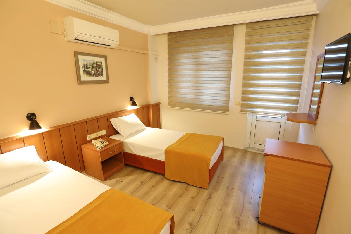 Une chambre d’hôtel avec deux lits, une commode en bois, une table de chevet avec une lampe, un téléphone et un téléviseur fixé au mur.