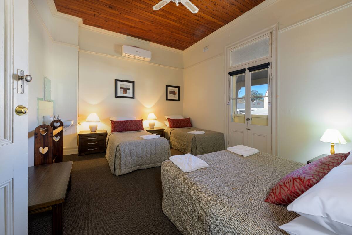 Ein Hotelzimmer mit zwei Einzelbetten, einer Holzbalkendecke, einem Fenster und einer Tür.