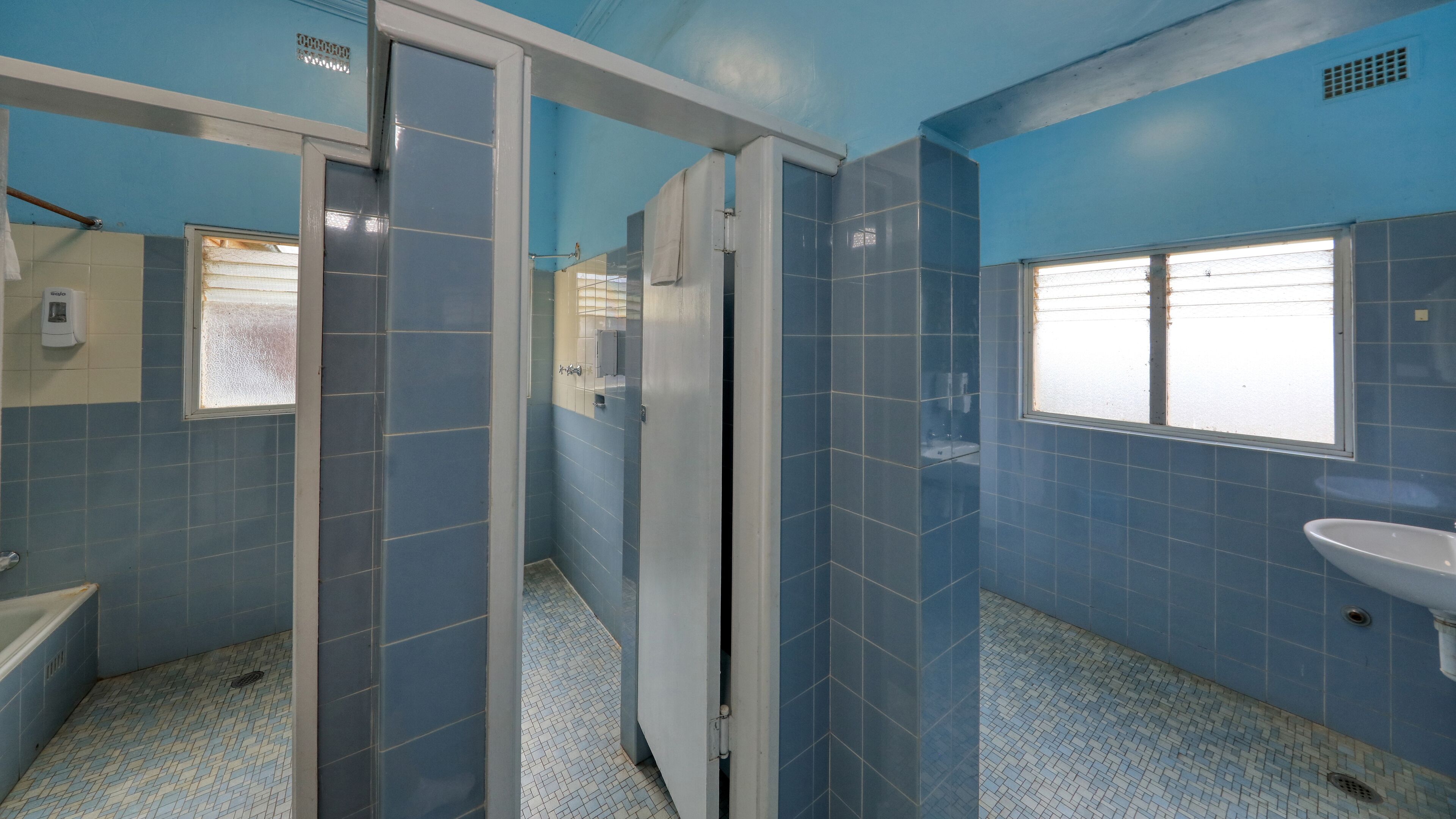 Une salle de bain avec des carreaux bleus, un lavabo blanc et une fenêtre avec des stores.