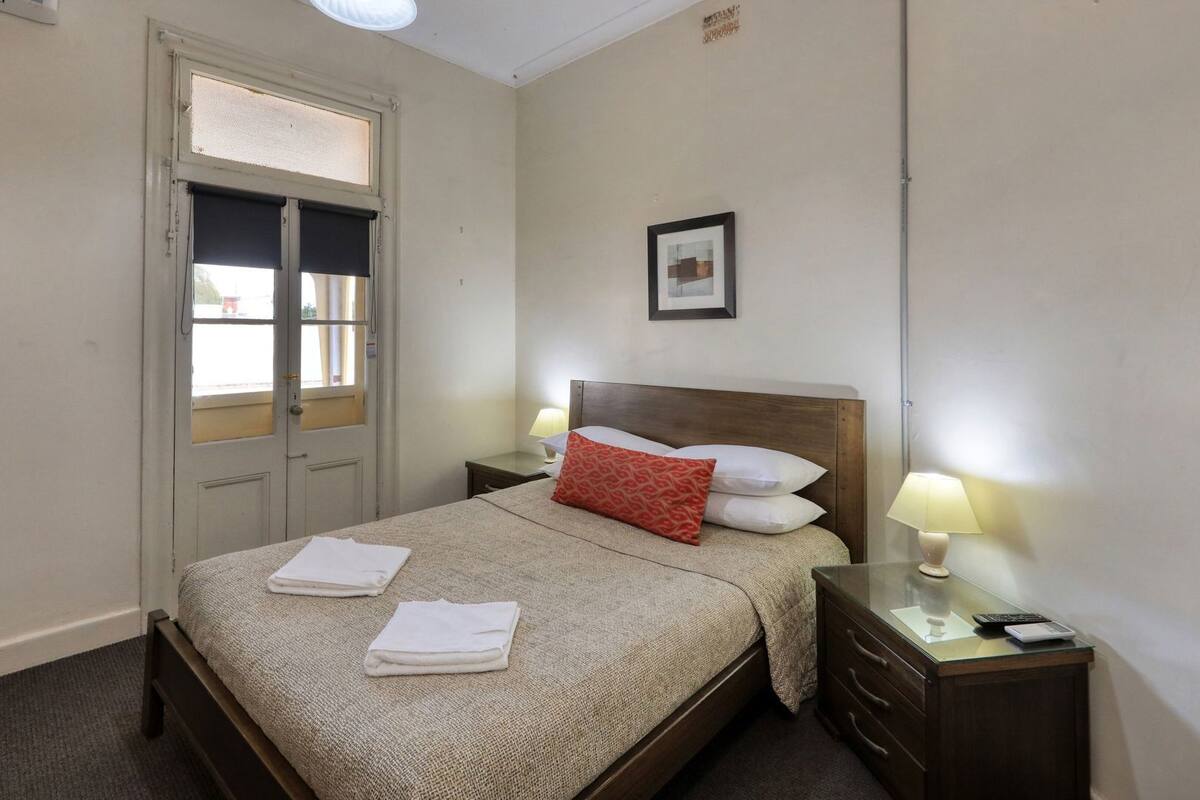 Ein Hotelzimmer mit einem Bett, zwei Nachttischen, einem Fenster und einem gerahmten Bild an der Wand.