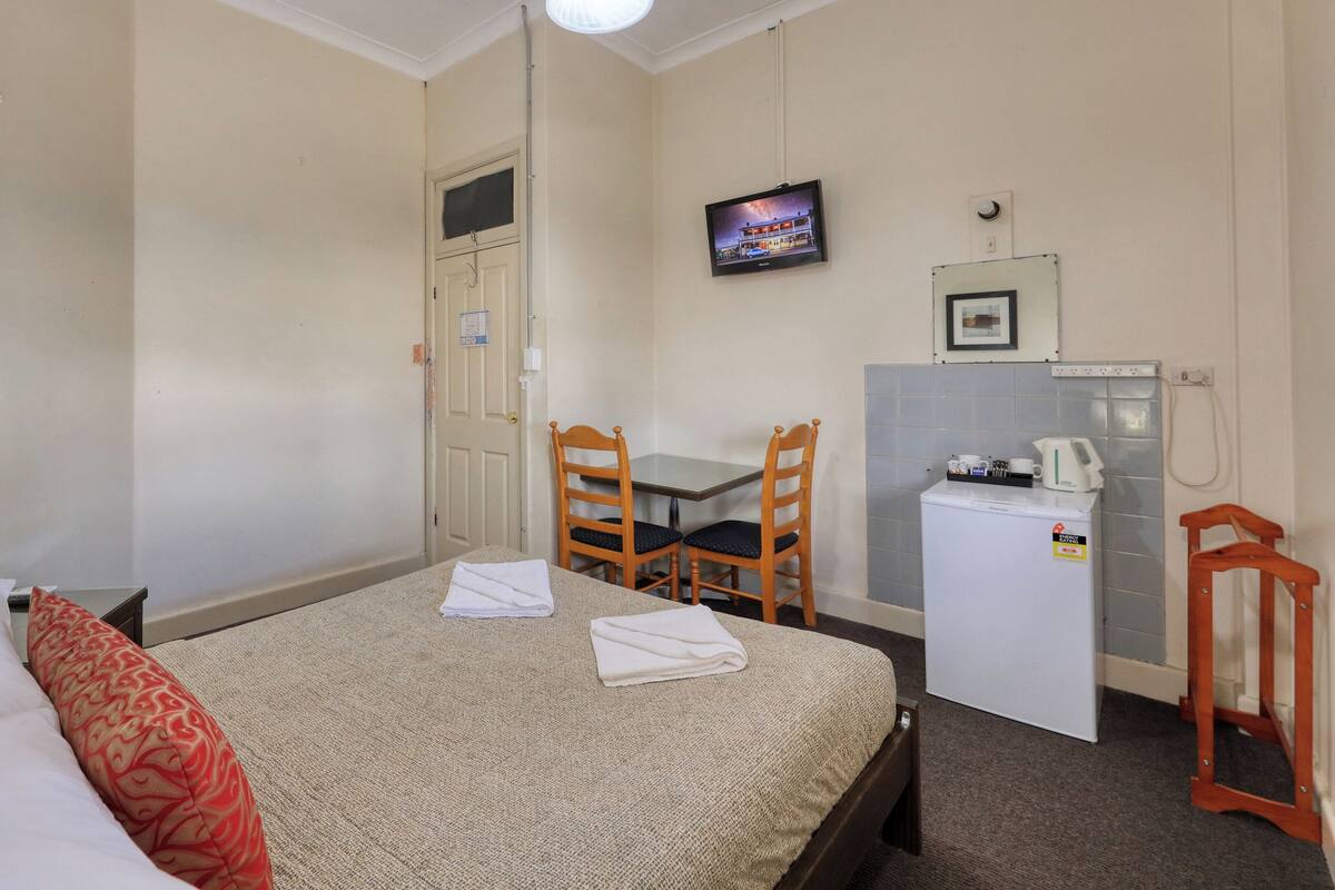 Ein Hotelzimmer mit einem Bett, einem Schreibtisch, einem Sessel, einem Fernseher, einem Kühlschrank und einem kleinen Tisch mit Wasserkocher.