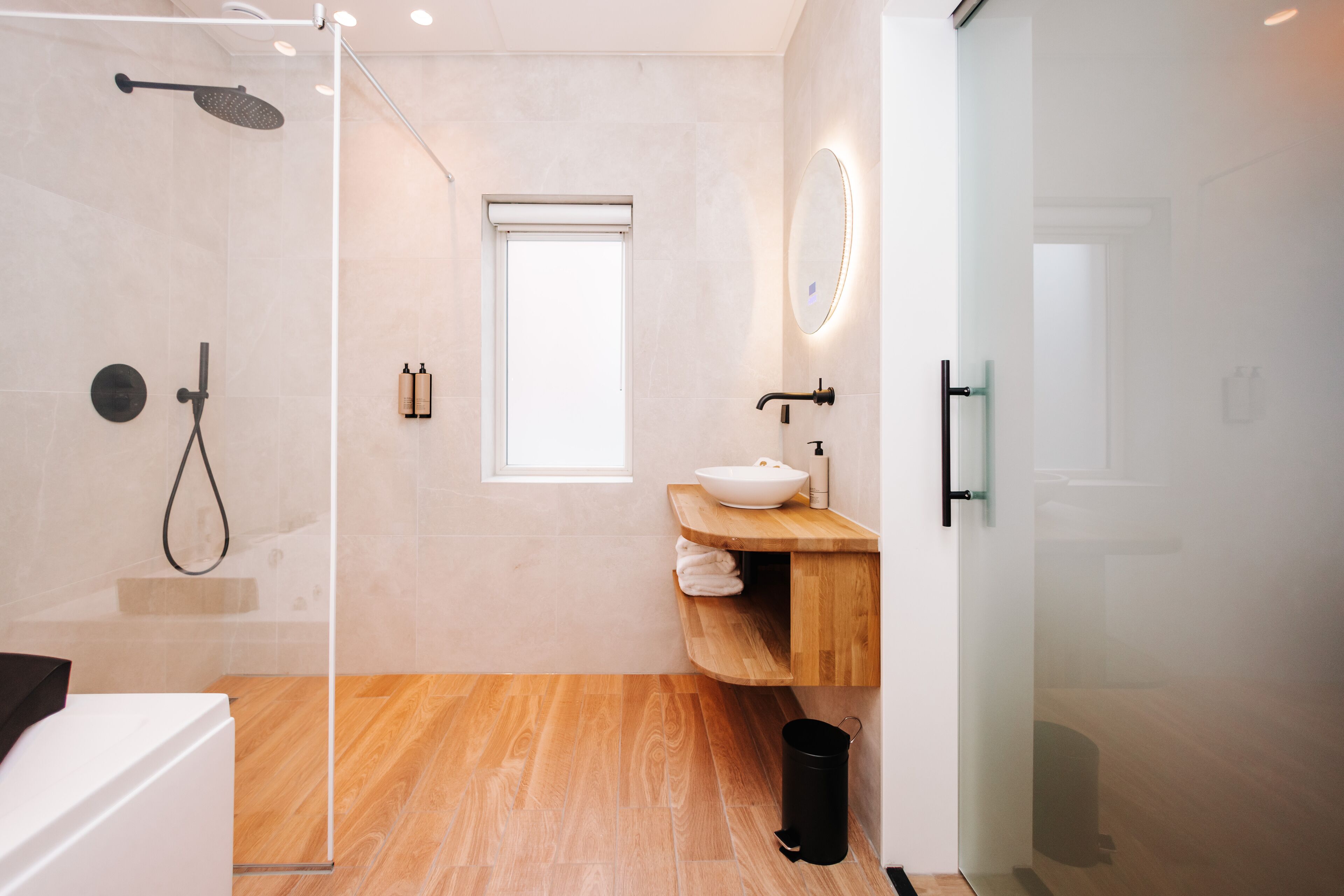 A modern bathroom with a glass shower enclosure, a wooden vanity with a sink, and a large mirror.