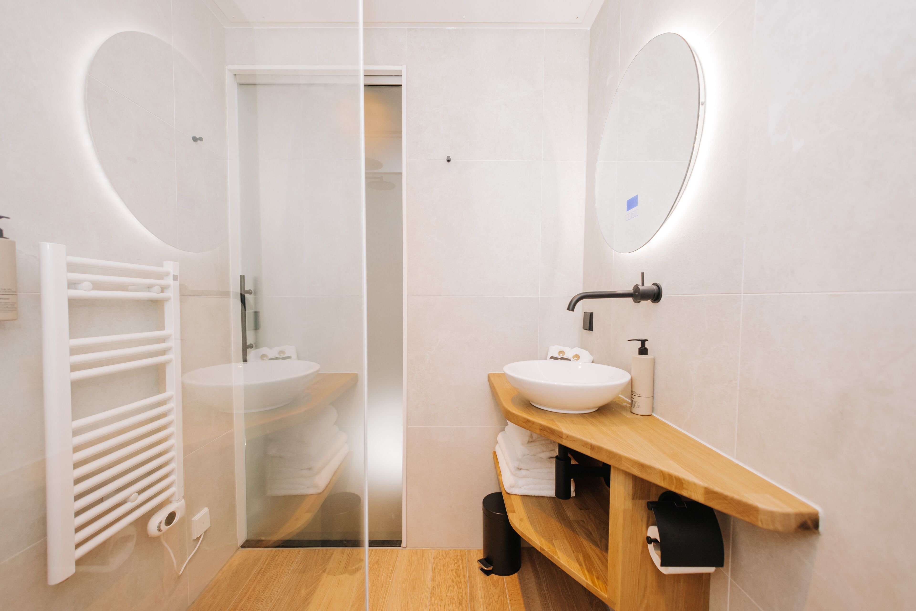 A modern bathroom with a glass partition, a wooden vanity, a white sink, and a towel rack.