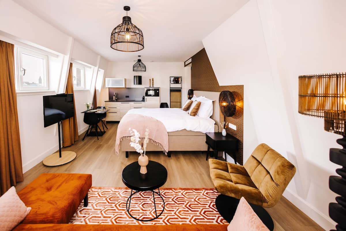 Una habitación de hotel moderna con cama, escritorio, silla, televisor y kitchenette.