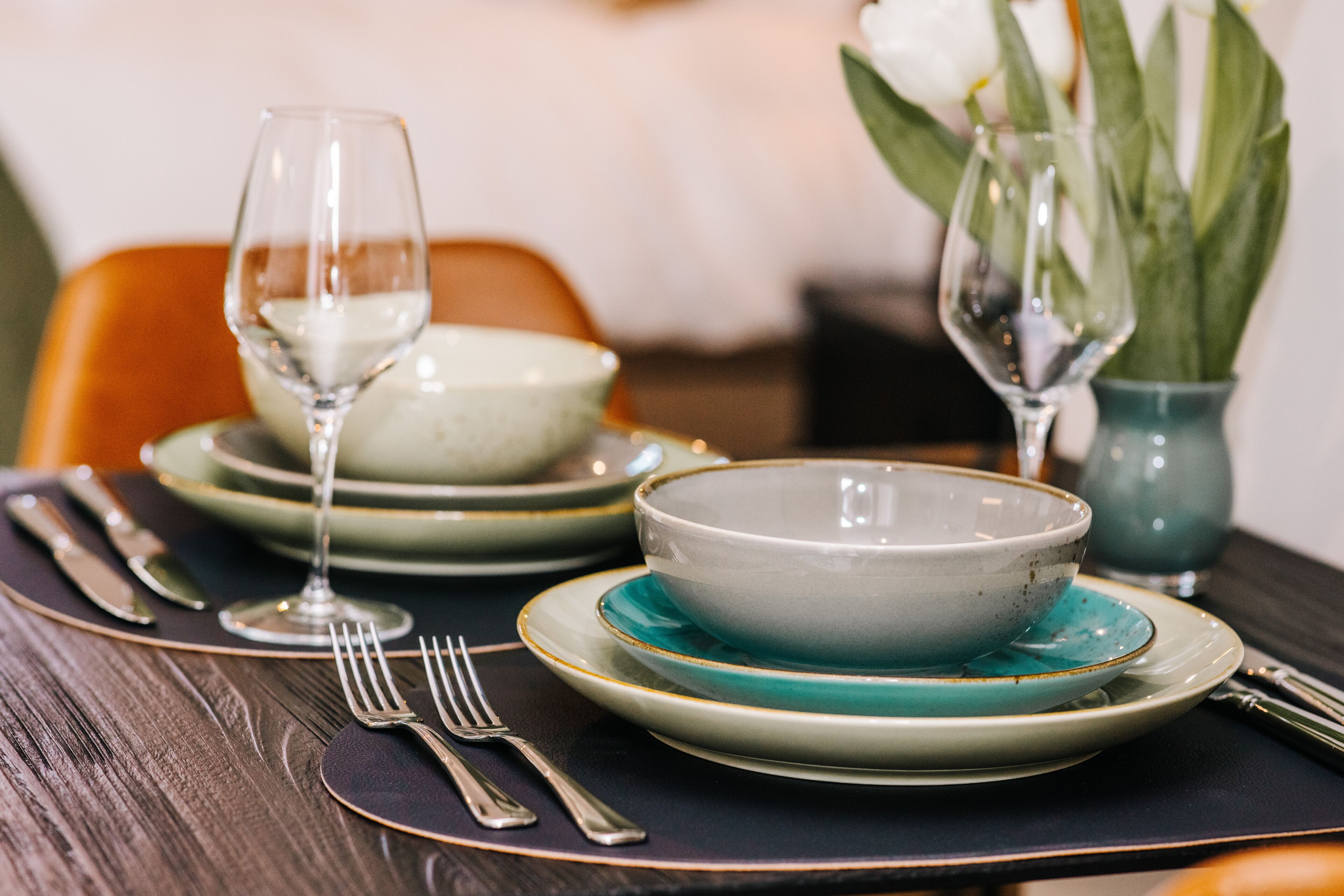 A dining table set with plates, bowls, cutlery, and a vase with flowers.