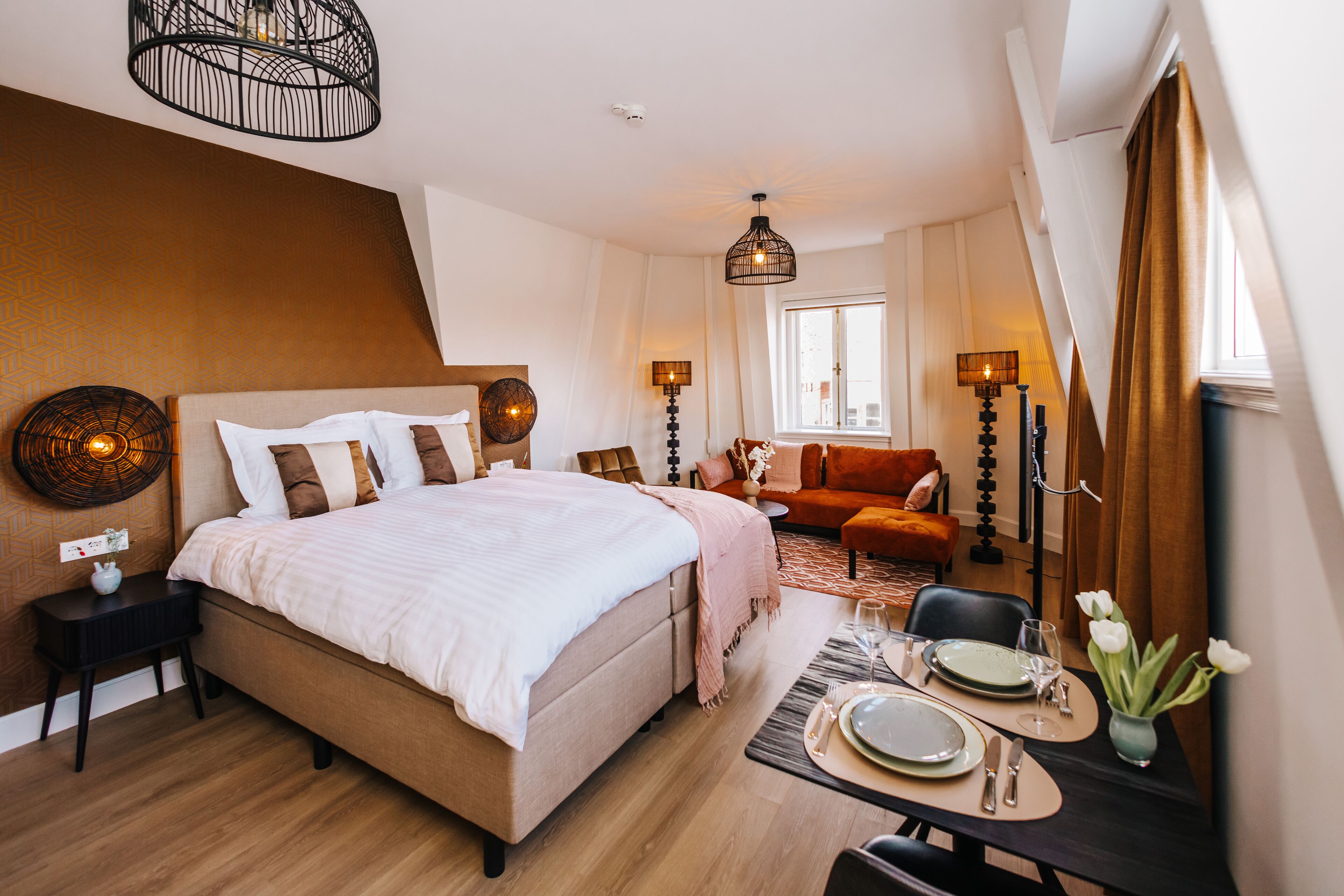 Ein modernes Schlafzimmer mit einem großen Bett, einem Esstisch für zwei Personen und einer gemütlichen Sitzecke mit einer Couch und Sesseln.