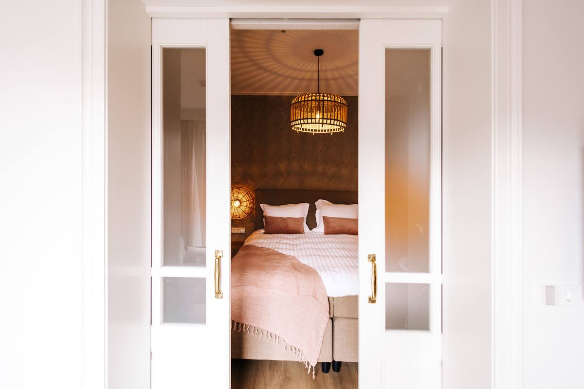 Un dormitorio con cama, lámpara colgante y puerta con paneles de vidrio.