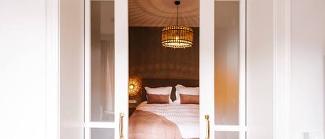 A bedroom with a bed, a hanging light fixture, and a door with glass panels.