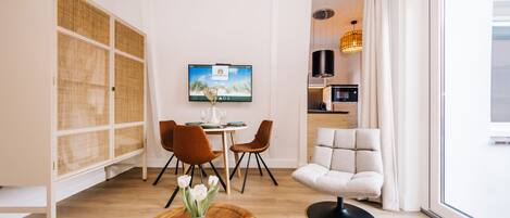 A modern living room with a dining area, a sofa, and a TV mounted on the wall.