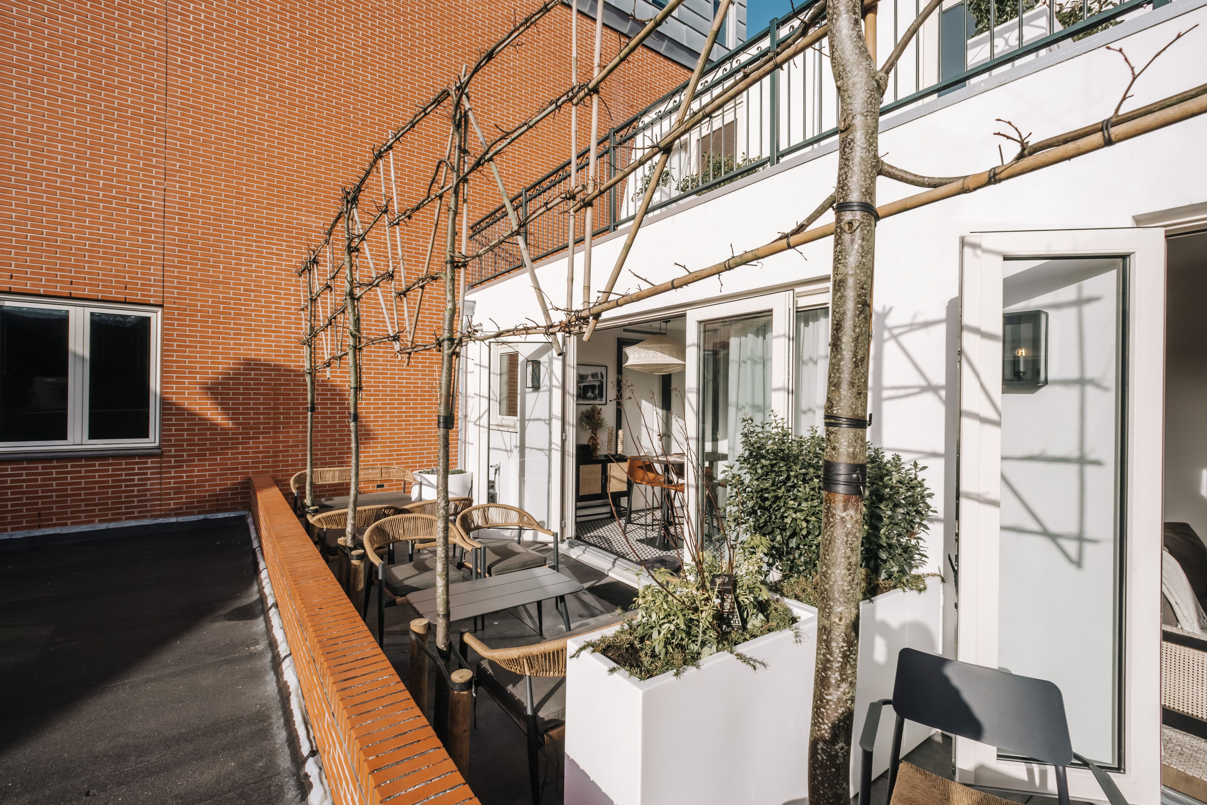 A rooftop patio with outdoor seating, a brick wall, and a white building with large windows.