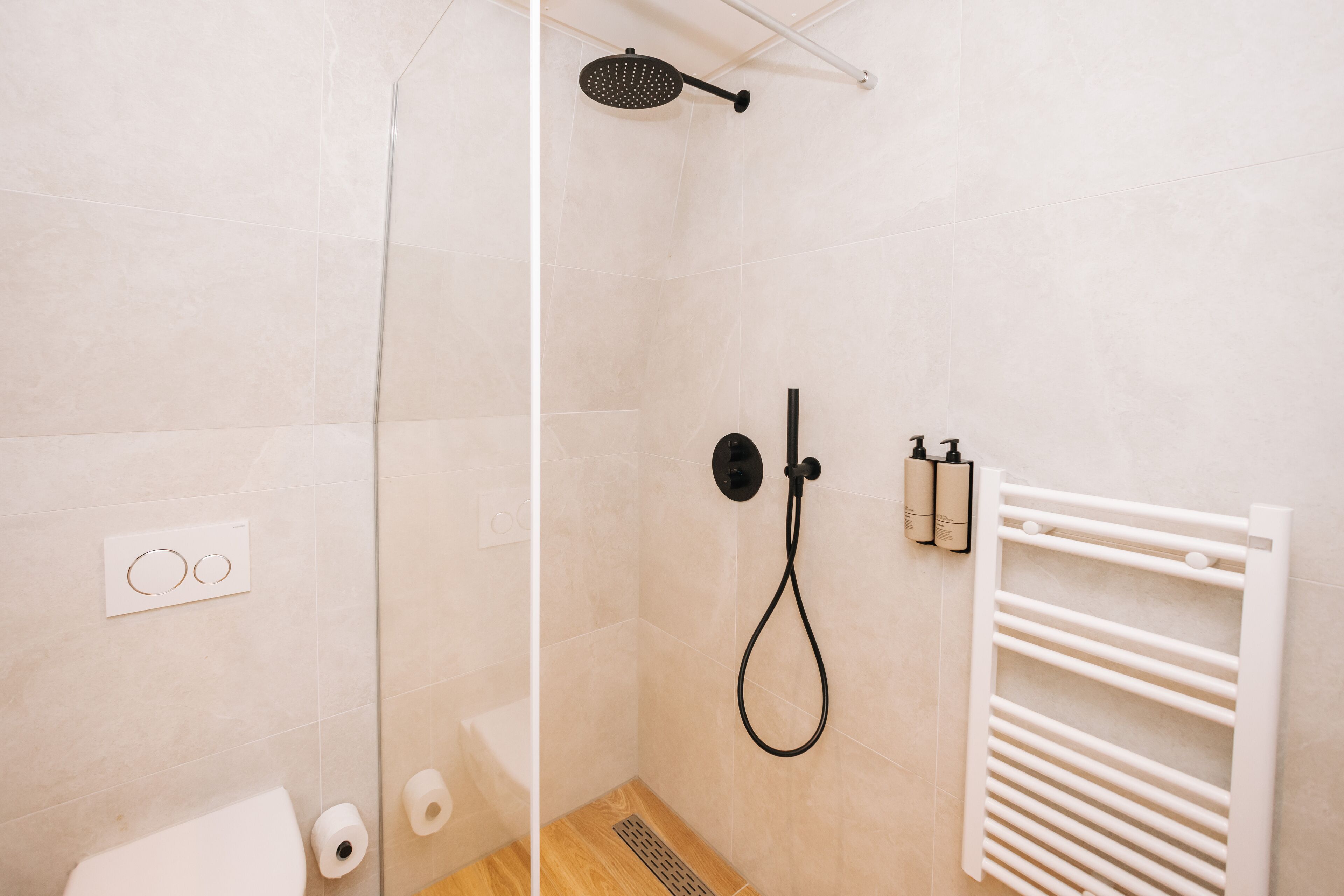 A modern bathroom with a glass shower enclosure, a white towel rack, and toiletries on the wall.