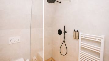 A modern bathroom with a glass shower enclosure, a white towel rack, and toiletries on the wall.