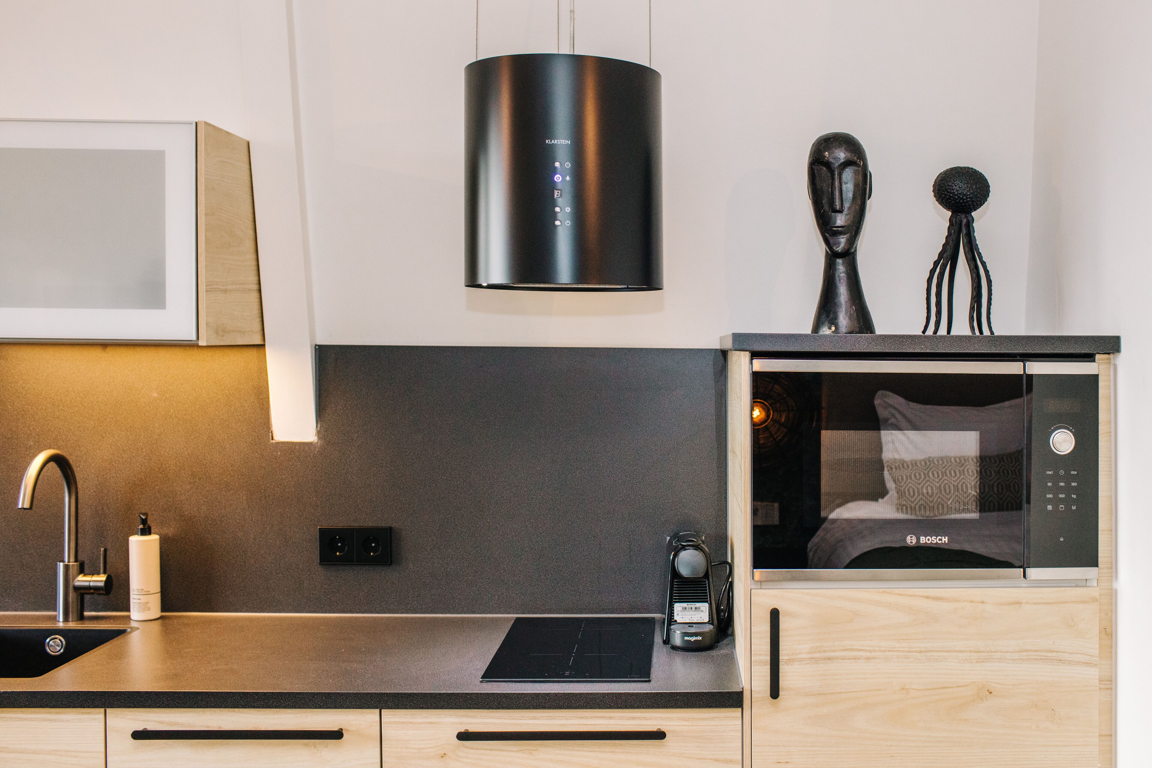 Una cocina moderna con un microondas Bosch, una campana extractora negra y un diseño minimalista.