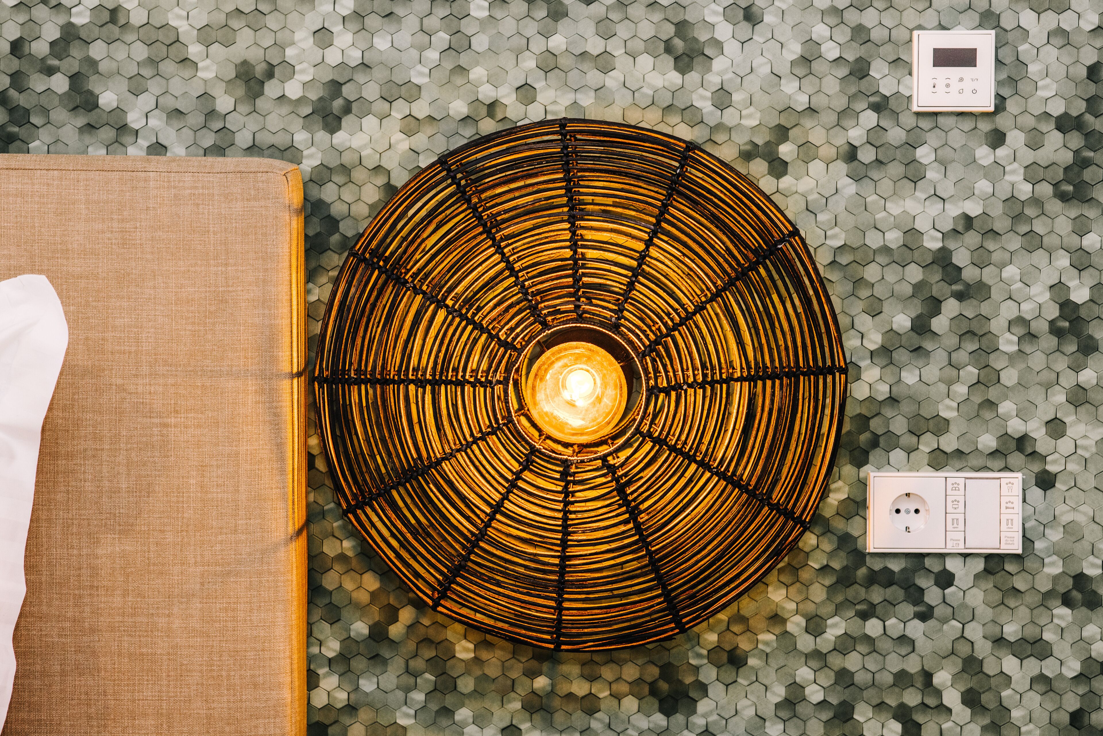A circular ceiling fan with a central light, a power outlet, and a switch on a hexagonal patterned wall.