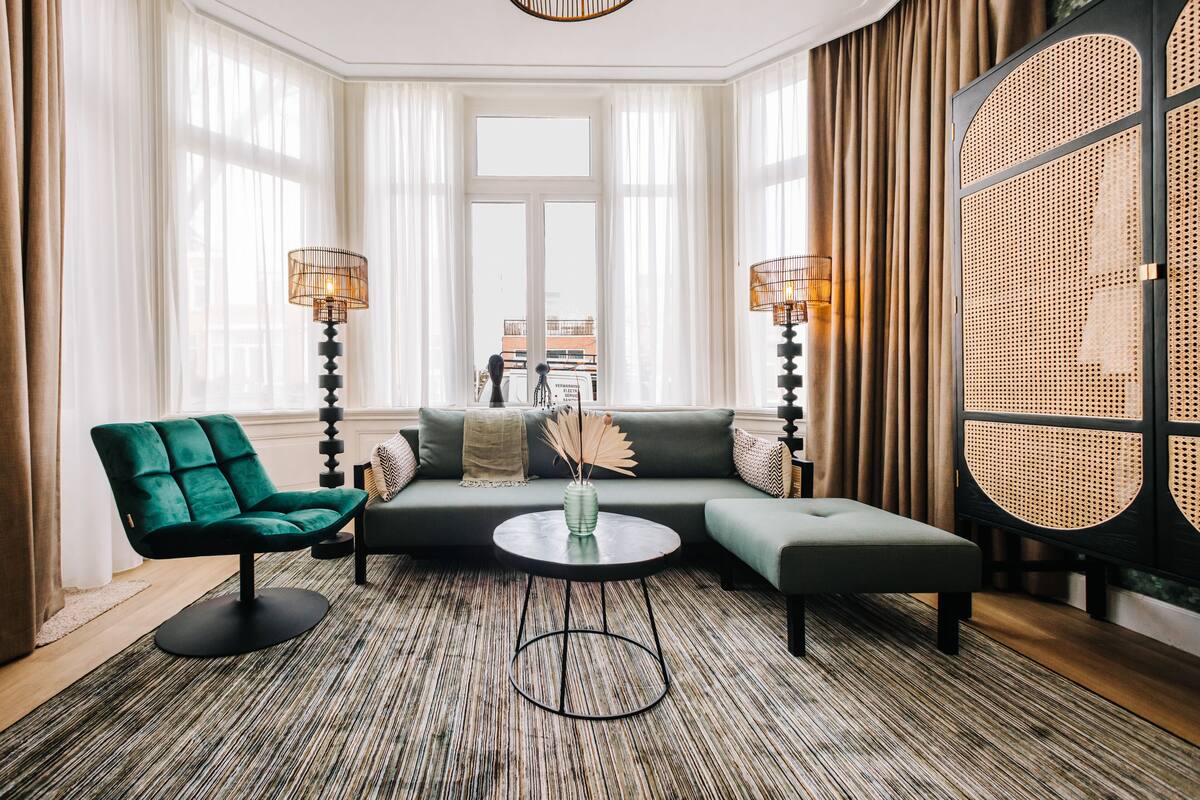 Una sala de estar moderna con un sofá modular, un sillón verde, una mesa de centro redonda y dos lámparas de pie.