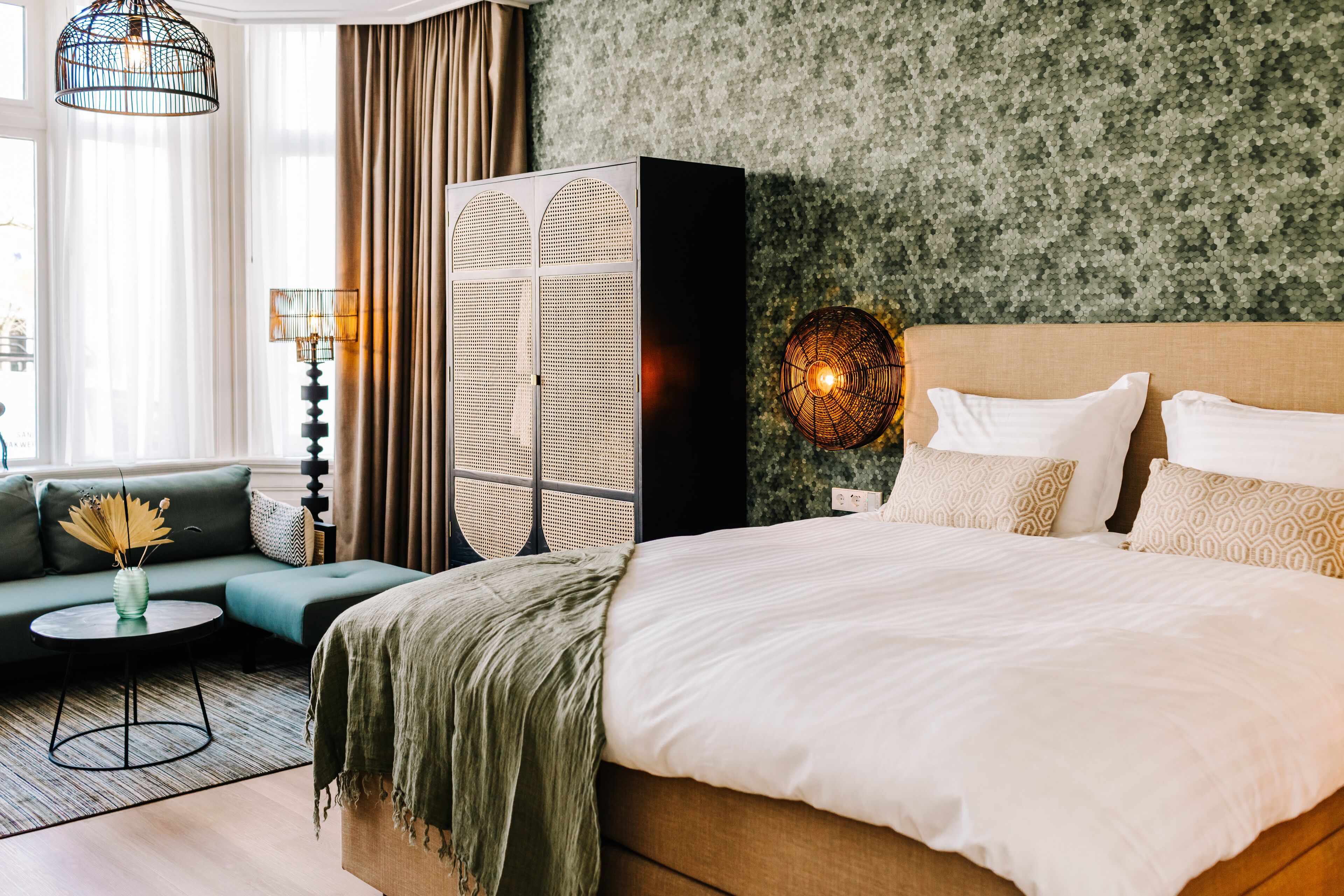 Ein Hotelzimmer mit einem großen Bett, einem grünen Sofa, einem kleinen runden Tisch und einer Zierleuchte.
