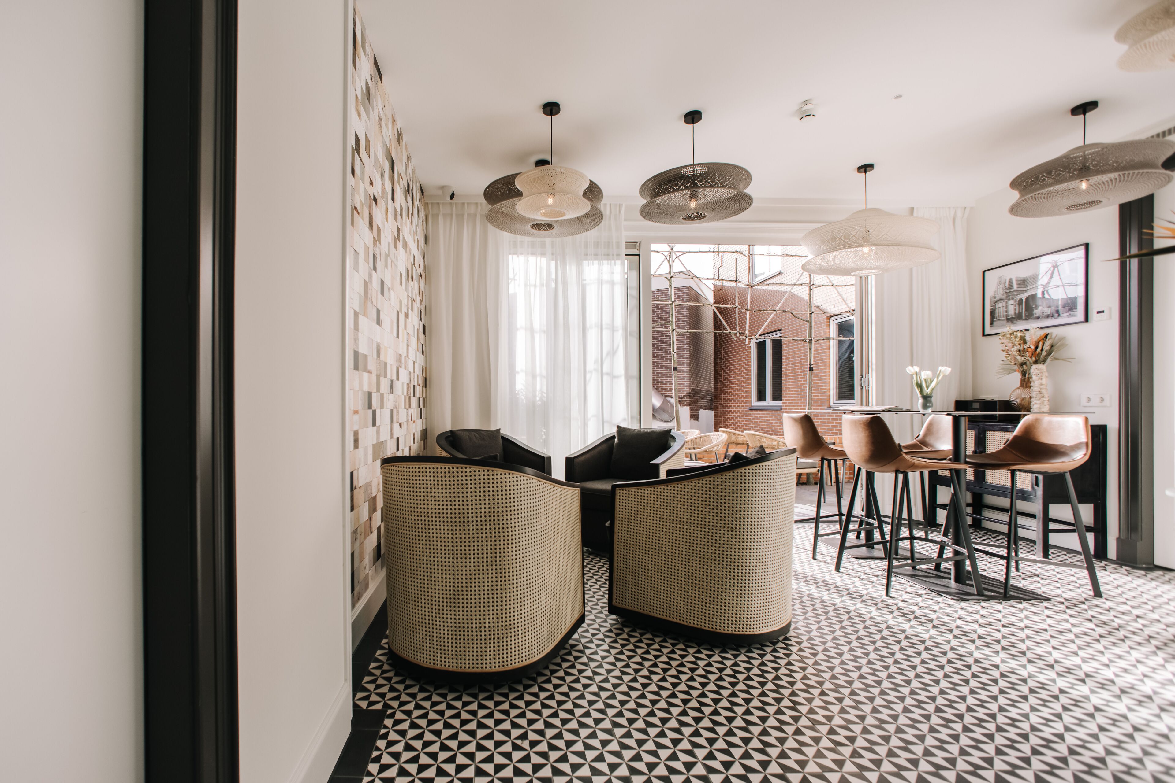 A modern interior with a geometric patterned floor, wicker furniture, and pendant lighting.