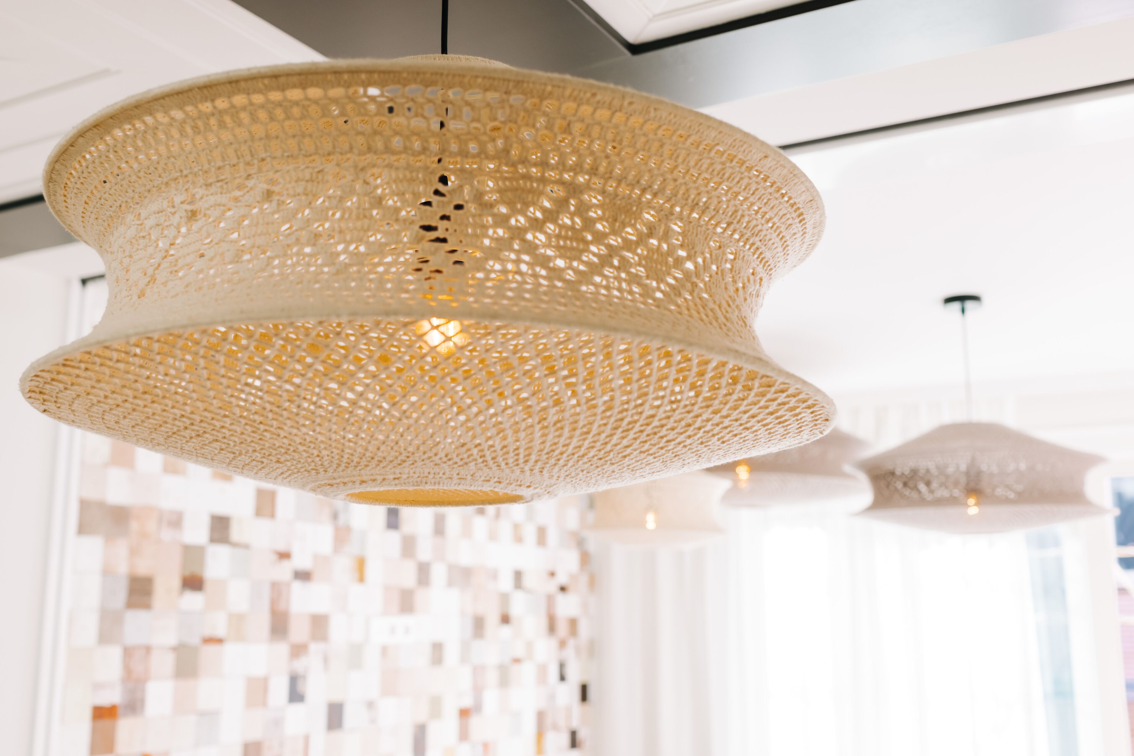 A modern interior with a woven pendant light fixture and a mosaic tile wall.