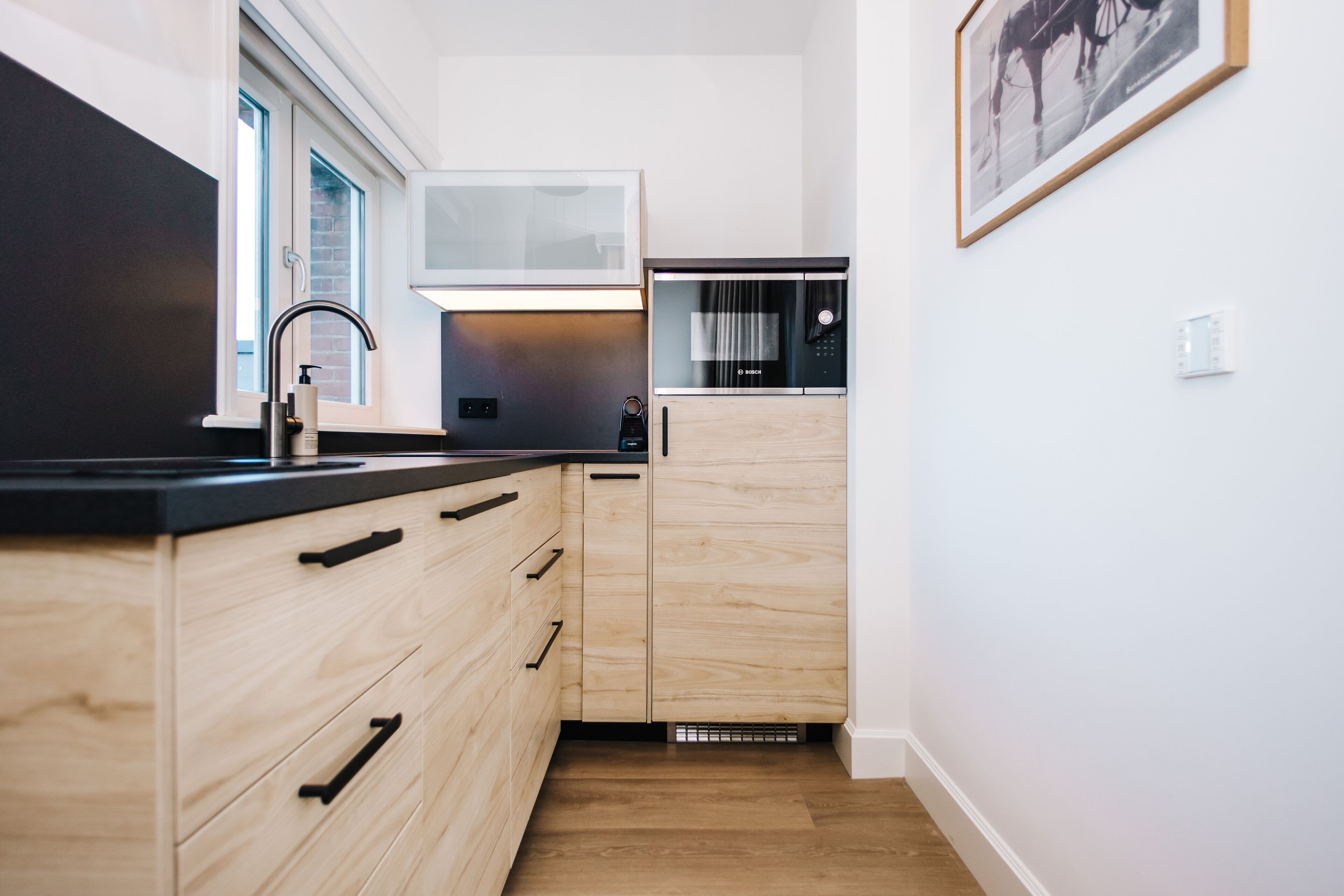 Une cuisine moderne avec des meubles en bois, un plan de travail noir et un four à micro-ondes encastré.