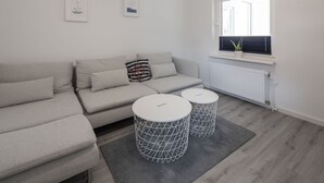 A modern living room with a grey sofa, two round white tables with wireframe bases, and a window with blinds.