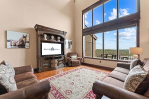 A spacious living room with a large window, a fireplace, and a television displaying a website.