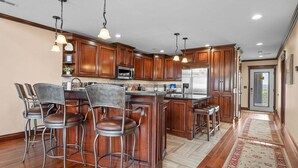 A kitchen with wooden cabinets, a stainless steel refrigerator, and a bar area with stools.