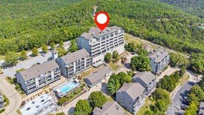 Un hotel de varios pisos con piscina en la azotea, rodeado de vegetación exuberante y terreno montañoso.