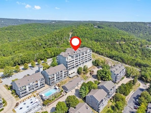 Ein mehrstöckiges Hotel mit Pool auf dem Dach, umgeben von üppiger Vegetation und hügeliger Landschaft.