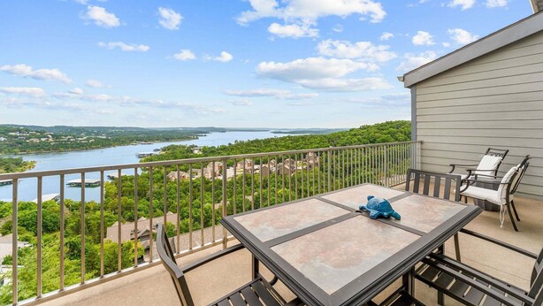 A balcony with a table and chairs, overlooking a river and greenery.