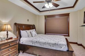 Ein Schlafzimmer mit einem hölzernen Bett, einem Nachttisch, einer Lampe, einem Deckenventilator und einem Fenster mit Jalousien.